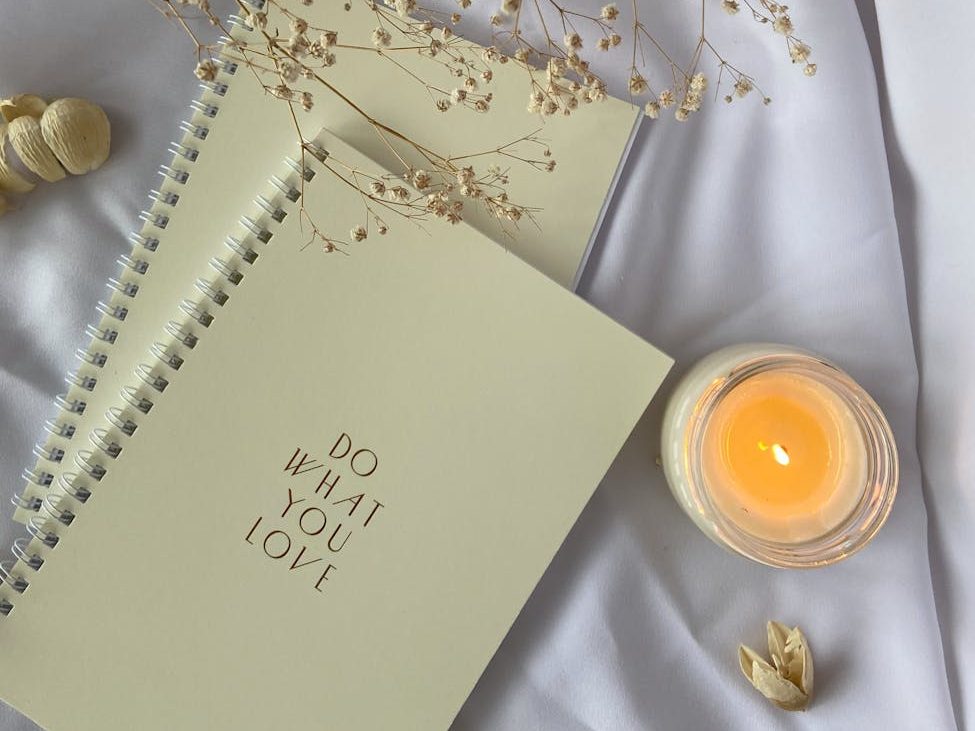 spiral notebooks placed on white cloth with burning candle
